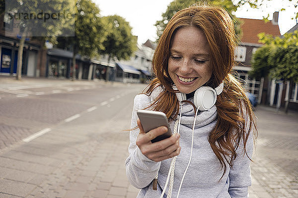 Redheaded woman using headphones and smartphone in the city