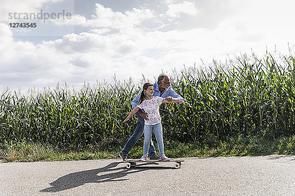 Mature man helping little girl to learn skateboarding