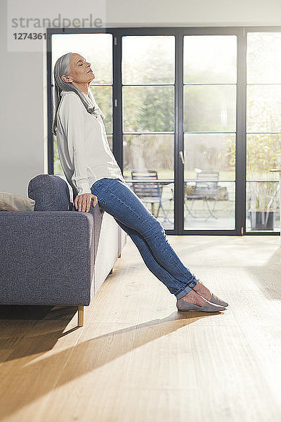 Senior woman standing by couch in living room  with eyes closed