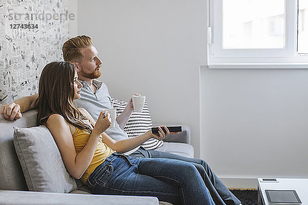 Couple sitting on couch drinking coffee and watching TV