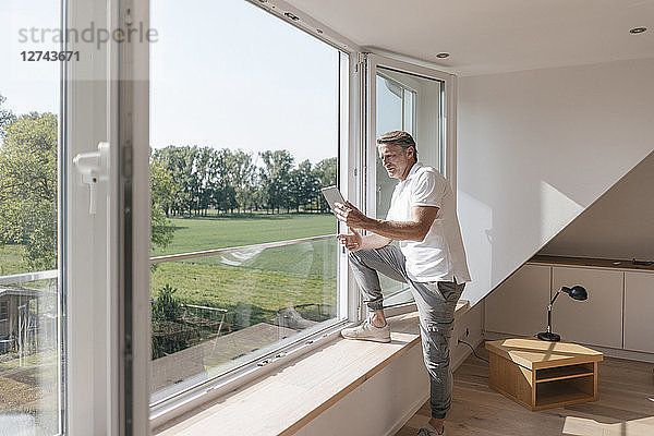 Mature man using tablet at the window in empty room