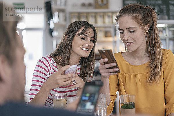Two girlfriends meeting in a coffee shop  using smartphones