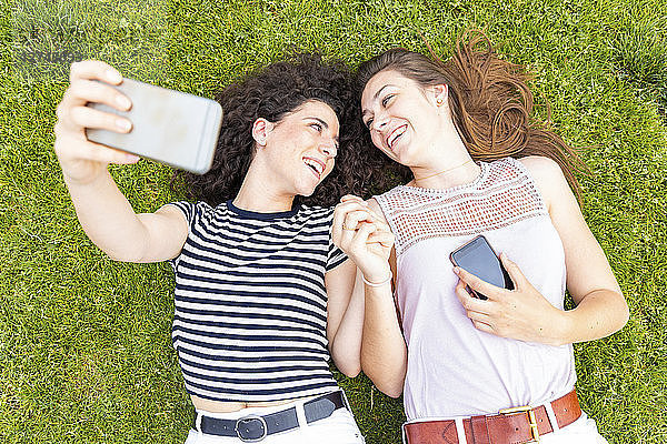 Two happy female friends lying down on grass taking a selfie