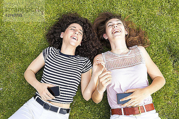 Two happy female friends lying down on grass and having fun