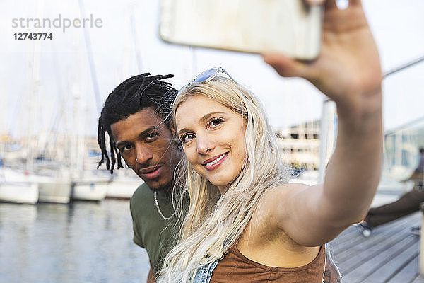 Portrait of multicultural young couple taking selfie with smartphone at harbour