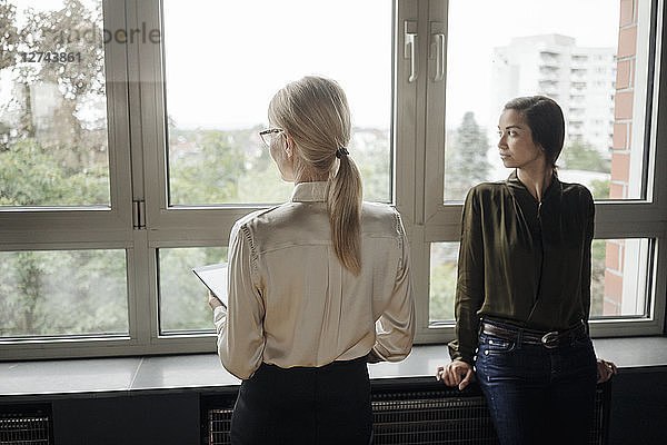 Two businesswomen in office looking out of window