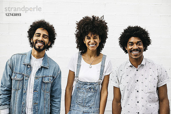 Group picture of three laughing friends in front of white wall