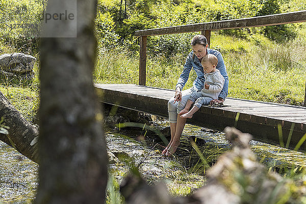 Mother and daughter sitting on wooden bridge  mountain stream