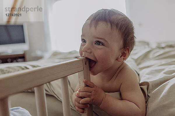 Laughing baby lying on bed  biting his cot