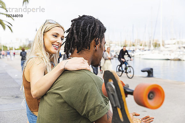 Multicultural young couple with longboard relaxing at harbour