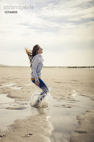 Happy woman having fun at the beach  jumping  splashing water