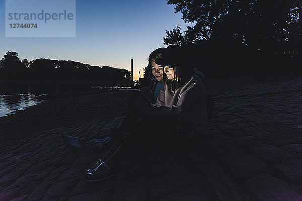 Young couple using tablet at the riverside in the evening