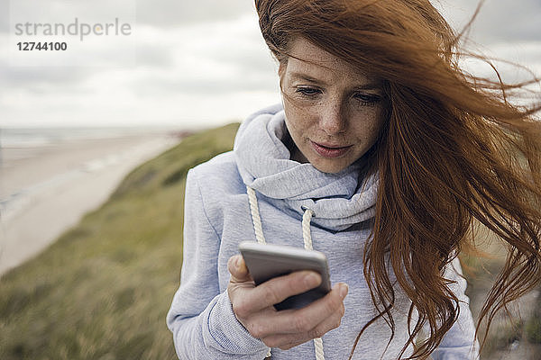 Redheaded woman using smartphone on the beach