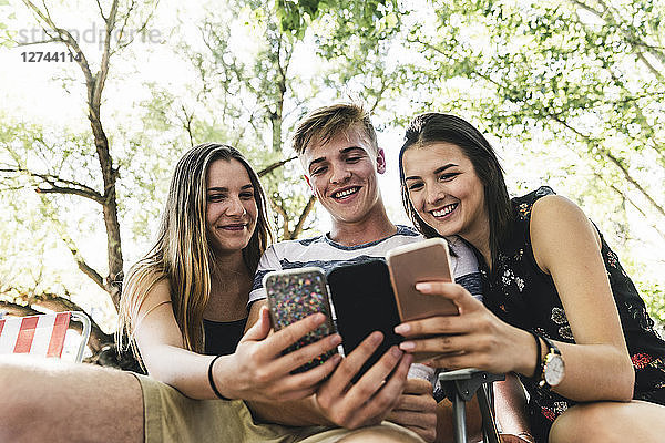Three happy friends looking at cell phones outdoors