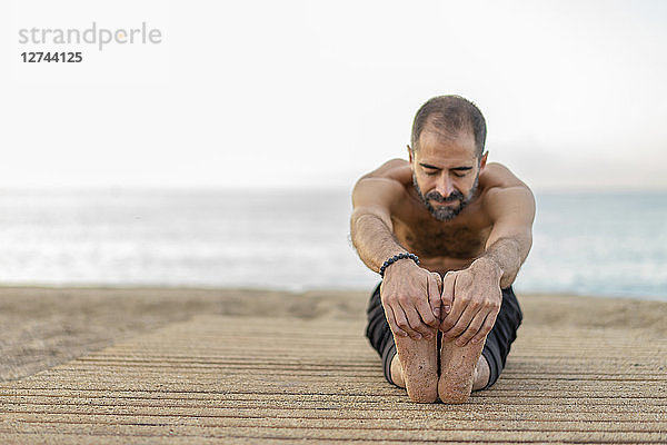 Spain. Man doing yoga on the beach in the evening  stretching legs