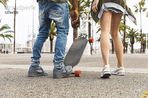 Spain  Barcelona  legs of multicultural young couple with longboard standing on promenade