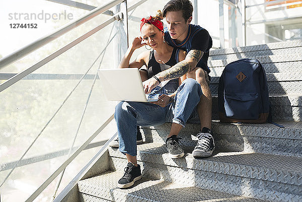 Young couple sitting on stairs using laptop