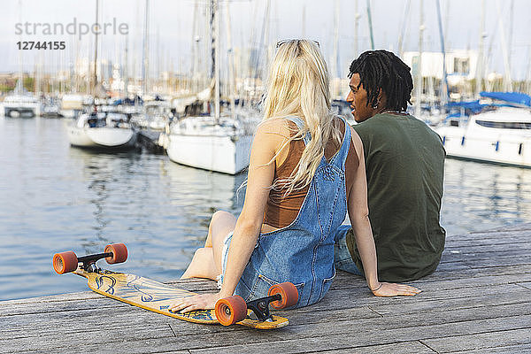 Spain  Barcelona  multicultural young couple with longboard relaxing at harbour