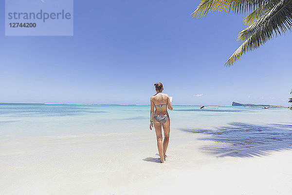 Mauritius  Cap Malheureux  young woman standing in water  reading a book  rear view