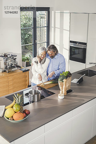 Happy senior couple preparing food in kitchen with online recipe