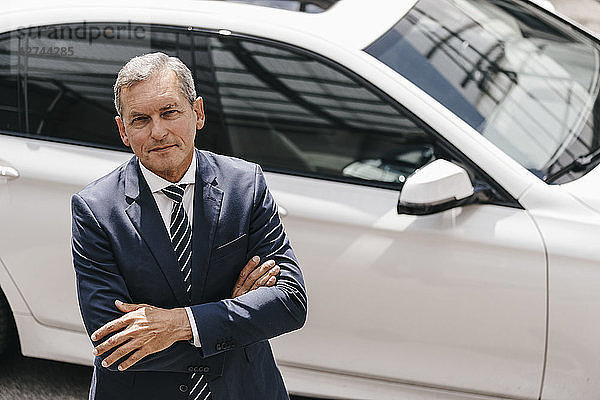 Portrait of mature businessman standing in front of car