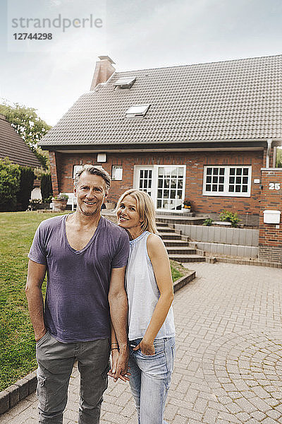 Portrait of smiling mature couple standing in front of their home