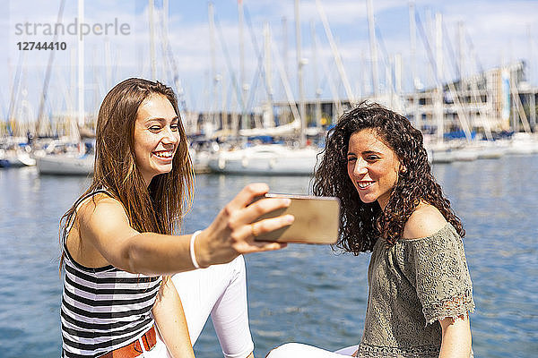 Two happy female friends taking a selfie at a marina