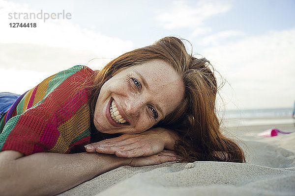 Redheaded woman lying in sand on the beach  with eyes closed