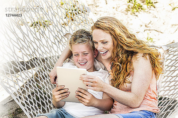 Happy mother and son in hammock looking at tablet