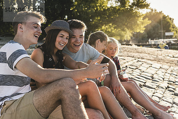 Group of friends sitting on cobblestones with refreshing drinks and cell phones