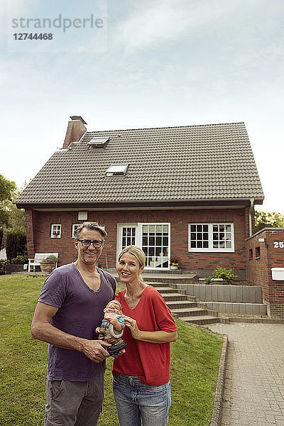 Portrait of smiling mature couple standing in front of their home holding garden gnome