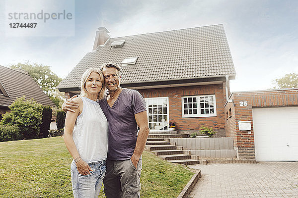 Portrait of smiling mature couple standing in front of their home