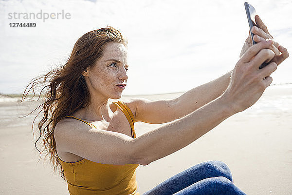 Redheaded woman taking smartphone selfie on the beach