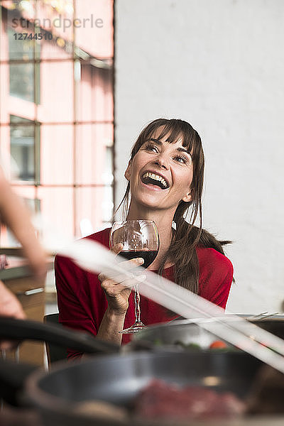 Woman sitting in kitchen  drinking red wine  watching man preparing food