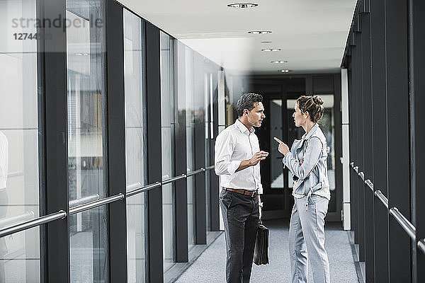 Businesswoman and businessman discussing in office passageway