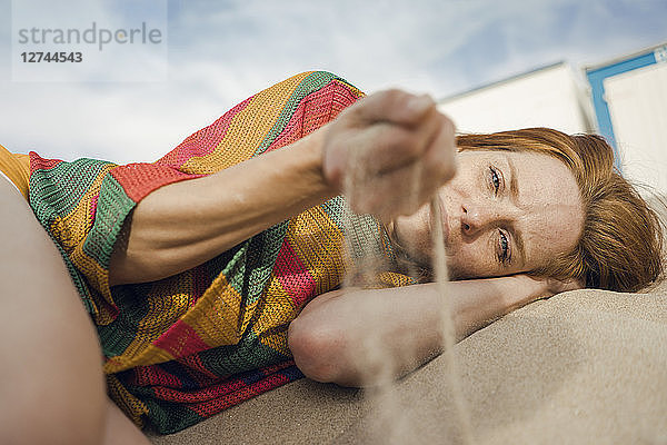 Redheaded woman lying on the beach  with sand trickling through her hand