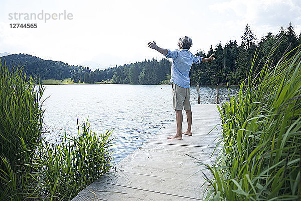 Germany  Mittenwald  mature man standing with arms outstretched on jetty at lake