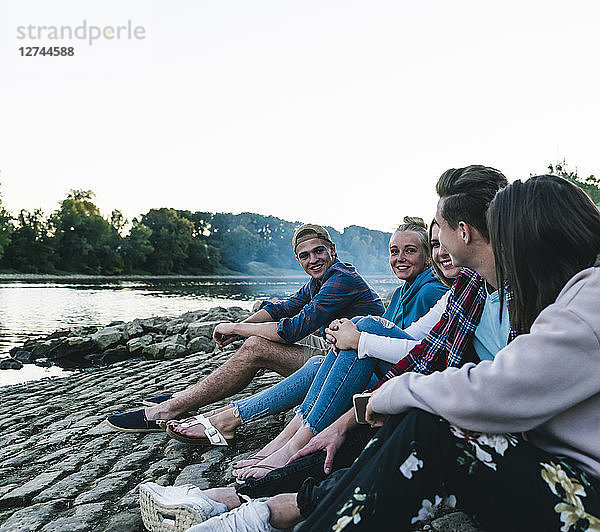 Group of friends sitting at the riverside in the evening