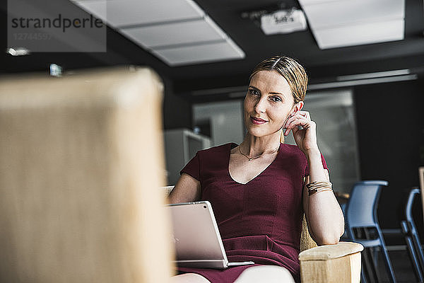 Businesswoman in office lounge wearing burgundy dress using laptop