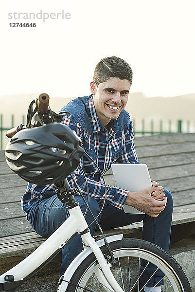 Portrait of smiling young man with folding bicycle and tablet