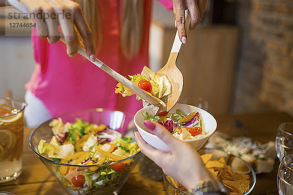 Close-up of woman dishing up salad for friend during dinner at home