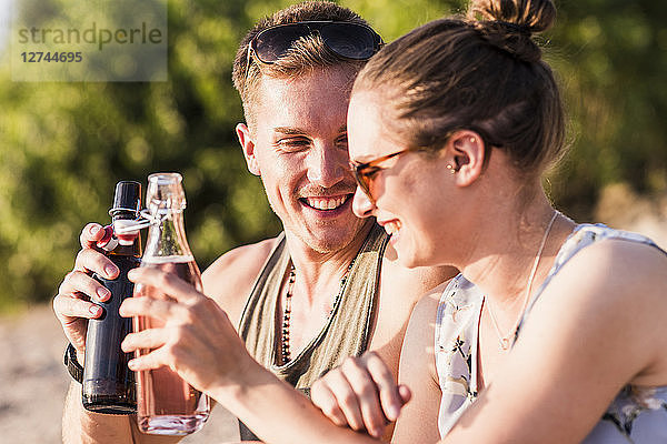 Happy young couple clinking bottles outdoors