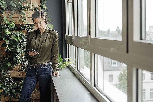Young woman in office at the window looking at cell phone
