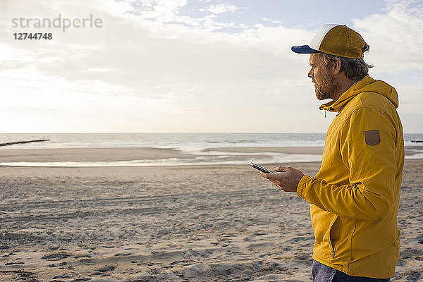 Man in yellow jacket  using smartphone on the beach