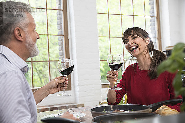 Happy couple sitting in kitchen  toasting with red wine  enjoying dinner