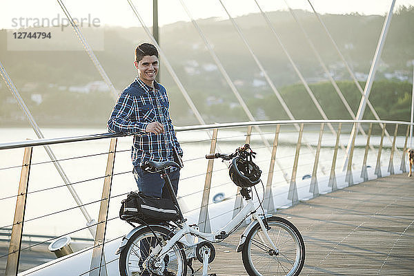 Portrait of smiling young man with folding bicycle on a bridge