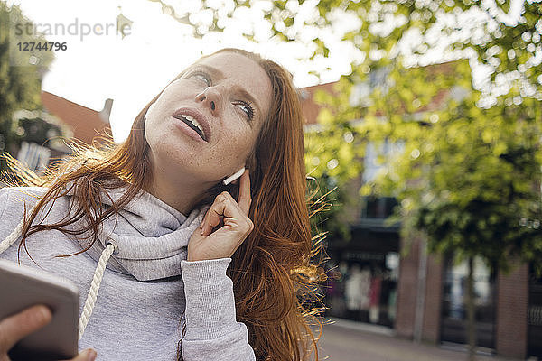 Redheaded woman using earbuds and smartphone
