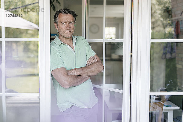 Portrait of serious mature man standing at French window