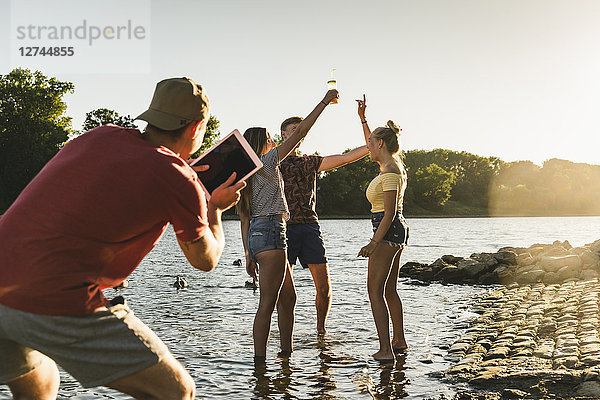 Group of happy friends with tablet in a river at sunset