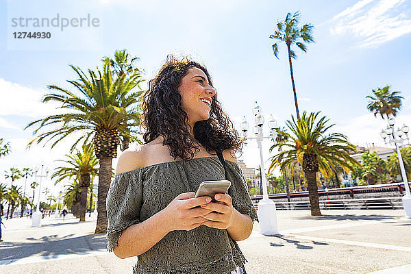 Smiling teenage girl holding smartphone at waterfront promenade